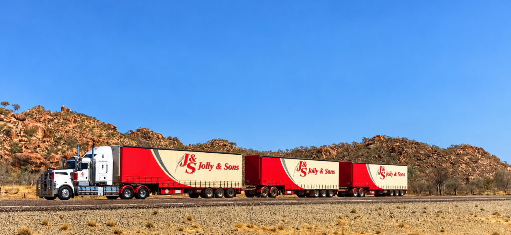 Jolly & Sons three-trailer road train with red and cream curtainsider trailers on a remote outback highway